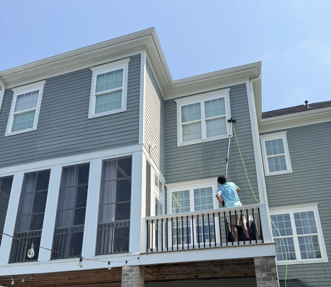 CrystalPane technician cleaning a third-story window with a water-fed pole, no ladder